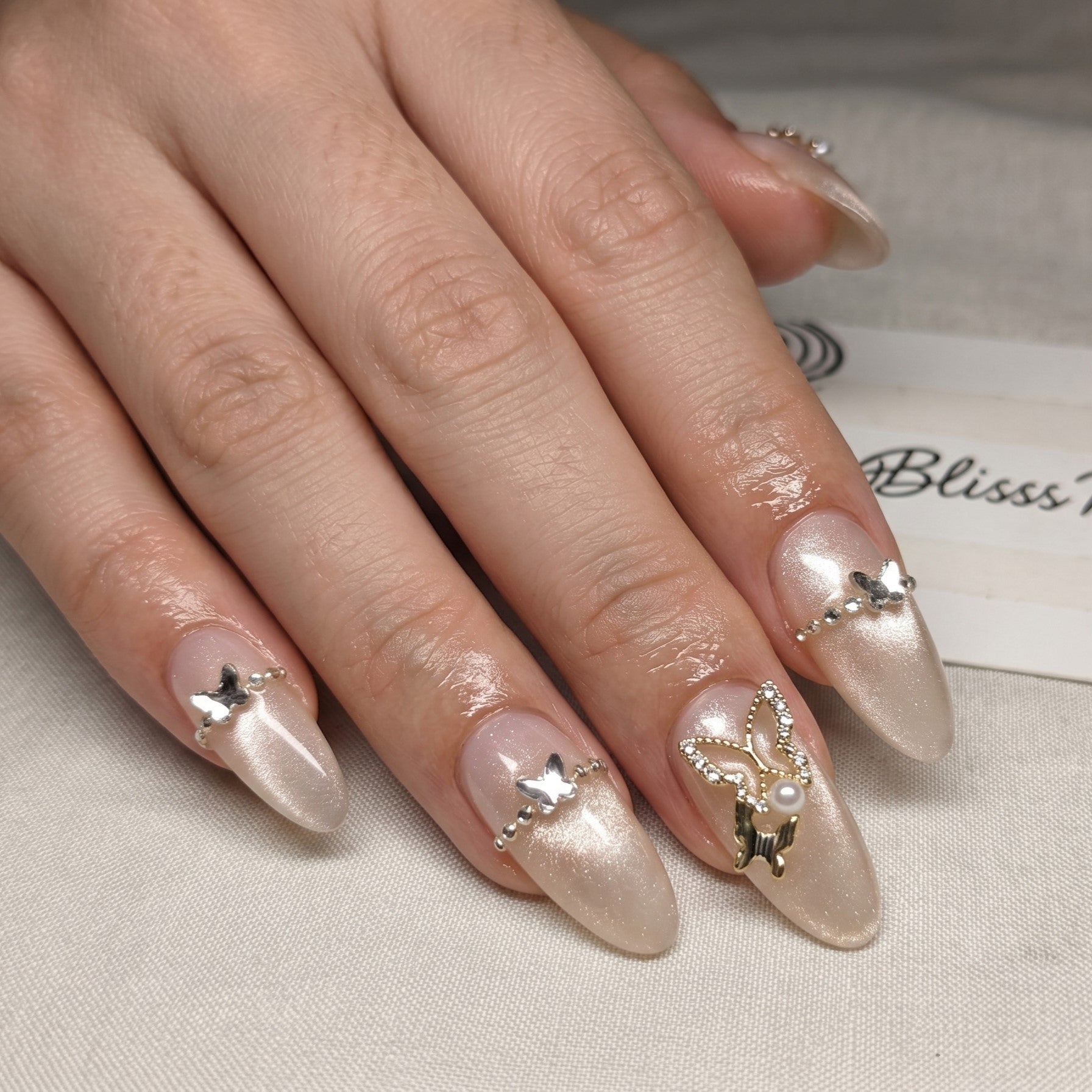 Blisss Nails Premium Handmade Nude Almond Fake Nails – Glossy Beige with Cat Eye Effect Artificial Reusable Press On Nails with Butterfly Charm & Crystal Chain Design | Elegant Salon Finish  10 pc Nail Set